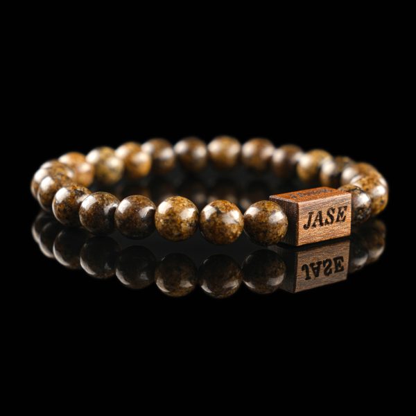 Handmade Botswana agate beaded bracelet with brown and grey bands and a dark wood engraved 'JASE' logo block, shown on a reflective black surface.