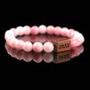 Handmade pink agate beaded bracelet with a dark wood engraved 'JASE' logo block, shown on a reflective black surface.