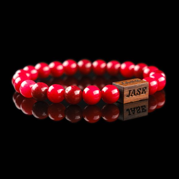 Handmade red agate beaded bracelet with a dark wood engraved 'JASE' logo block, shown on a reflective black surface.