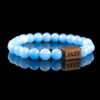 Handmade light blue aquamarine beaded bracelet with a dark wood engraved 'JASE' logo block, shown on a reflective black surface.