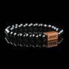 Handmade polished black onyx beaded bracelet with a dark wood engraved 'JASE' logo block, shown on a reflective black surface.