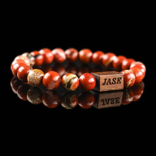 Handmade Picture jasper beaded bracelet with earthy brown, tan, and red patterns and a dark wood engraved 'JASE' logo block, shown on a reflective black surface.