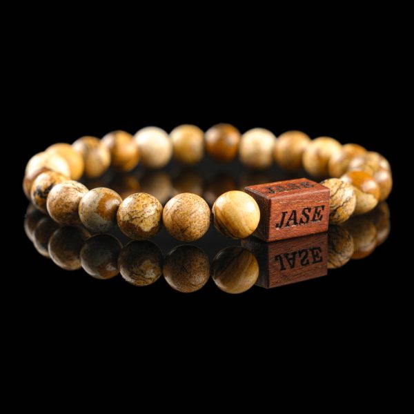 Handmade picture jasper beaded bracelet with sandy brown and tan landscape patterns and a dark wood engraved 'JASE' logo block, shown on a reflective black surface.
