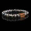 Handmade labradorite beaded bracelet with grey and black stones showing a subtle flash of labradorescence, with a dark wood engraved 'JASE' logo block, on a reflective black surface.