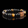 Handmade bracelet with black lava stone, polished onyx, and golden-brown tiger's eye beads, featuring a dark wood engraved 'JASE' logo block on a reflective black surface.