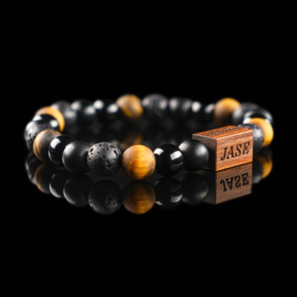 Handmade bracelet with black lava stone, polished onyx, and golden-brown tiger's eye beads, featuring a dark wood engraved 'JASE' logo block on a reflective black surface.