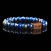 Handmade deep blue lazurite beaded bracelet with golden pyrite flecks and a dark wood engraved 'JASE' logo block, shown on a reflective black surface.