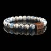 Handmade sodalite beaded bracelet with blue and black spots on a light grey stone matrix, featuring a dark wood engraved 'JASE' logo block on a reflective black surface.