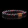 Handmade bracelet with polished black and deep red tourmaline beads, featuring a dark wood engraved 'JASE' logo block on a reflective black surface.