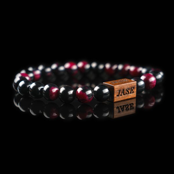 Handmade bracelet with polished black and deep red tourmaline beads, featuring a dark wood engraved 'JASE' logo block on a reflective black surface.