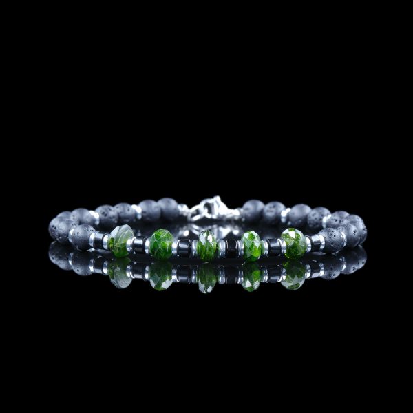 The Magnate bracelet by onejase with faceted green emerald beads, black lava stone, and hematite spacers, featuring a stainless steel clasp, on a black reflective surface.